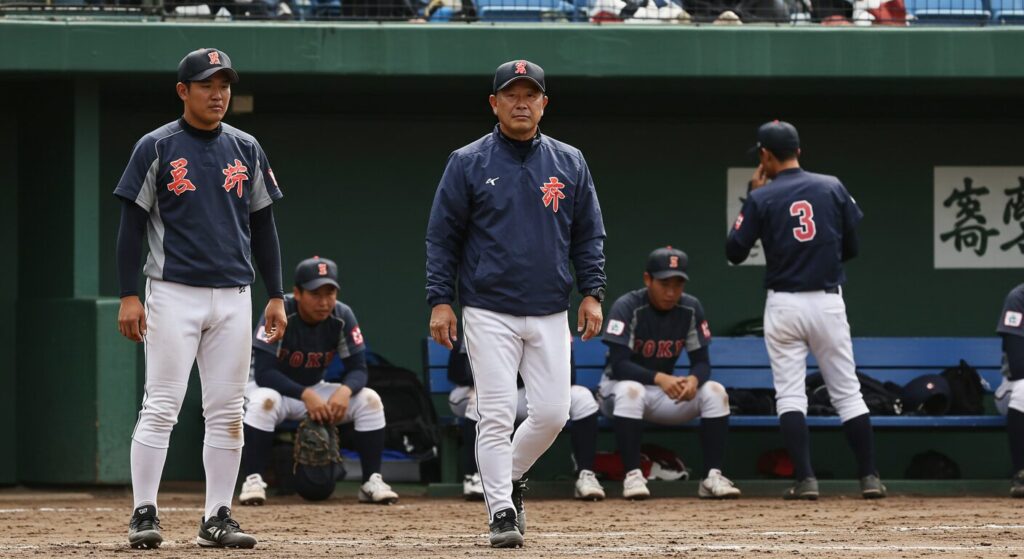 試合に敗れ、ベンチでうなだれる少年野球の選手たちと、それを見つめる監督。