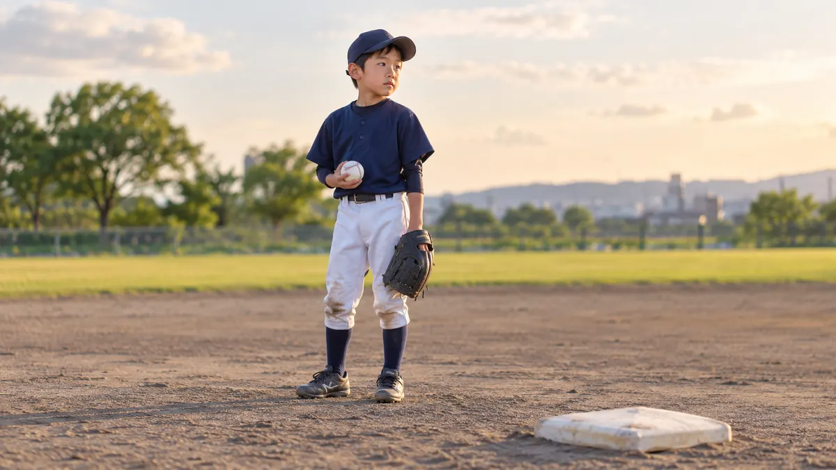 練習の合間にボールを持ち、塁を見つめる少年のイメージ（生成AIによる画像）