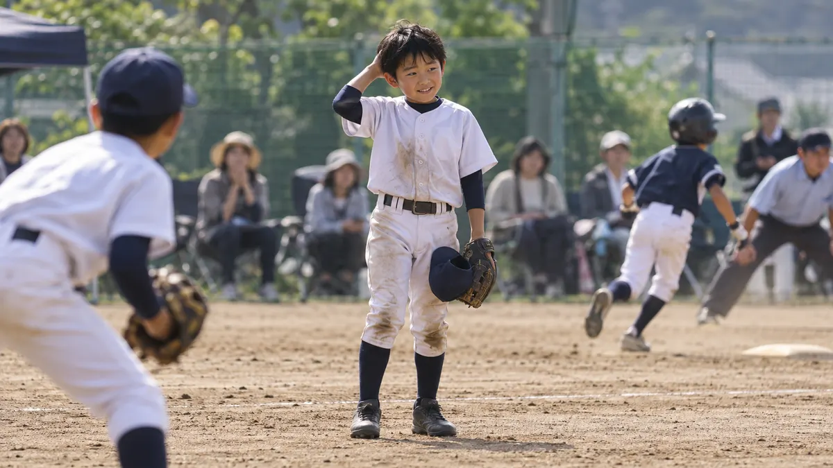 ��スの直後、帽子を手に少し笑う少年選手のイメージ（生成AIによる画像）